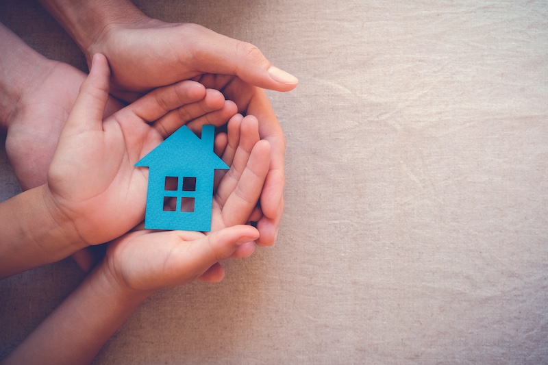 Adult and child hands holding paper house, family home and real estate concept